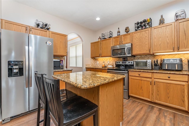 kitchen with a breakfast bar, a center island, hardwood / wood-style flooring, light stone countertops, and appliances with stainless steel finishes