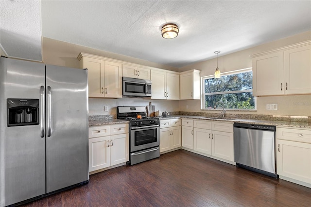 kitchen with stainless steel appliances, dark hardwood / wood-style flooring, light stone countertops, pendant lighting, and sink