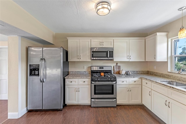 kitchen featuring appliances with stainless steel finishes, decorative light fixtures, dark hardwood / wood-style flooring, light stone countertops, and sink