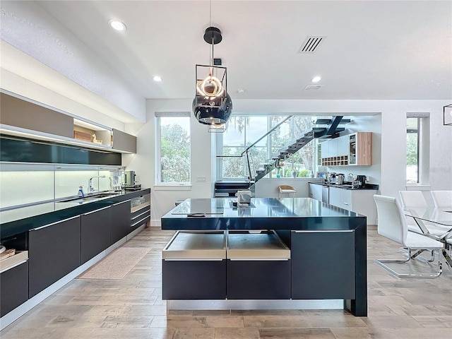 kitchen featuring stainless steel counters, a spacious island, light hardwood / wood-style floors, ceiling fan, and decorative light fixtures