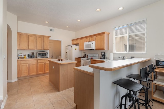 kitchen with white appliances, a breakfast bar, a center island, and kitchen peninsula