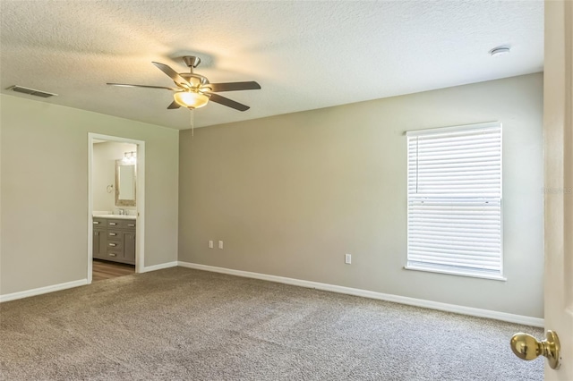 unfurnished bedroom with ensuite bathroom, carpet, ceiling fan, and a textured ceiling