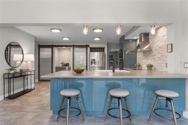 kitchen with stainless steel built in fridge, kitchen peninsula, a breakfast bar, a barn door, and wall chimney exhaust hood