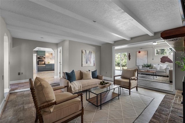 living room featuring beamed ceiling, a textured ceiling, light hardwood / wood-style floors, and ceiling fan