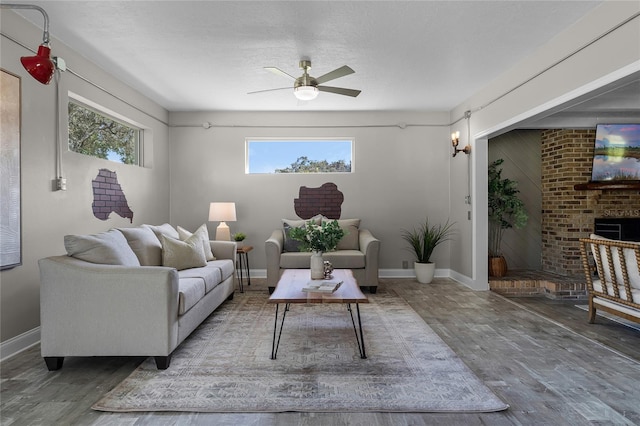 living room featuring ceiling fan, hardwood / wood-style flooring, a textured ceiling, and a brick fireplace