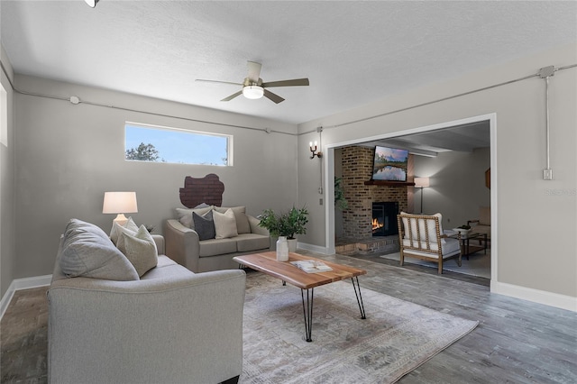 living room featuring a textured ceiling, wood-type flooring, a fireplace, and ceiling fan