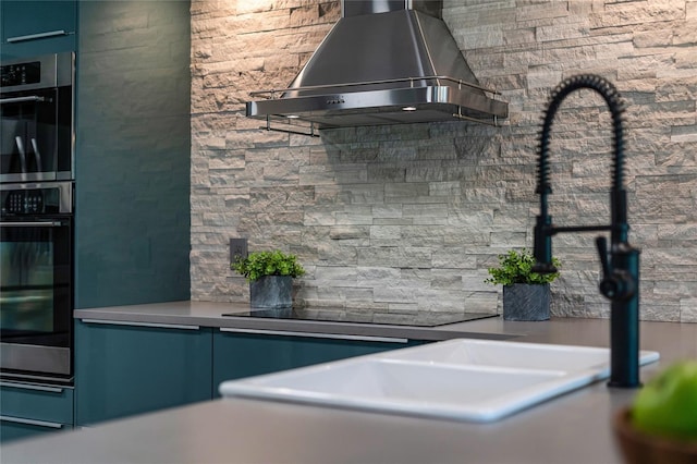 kitchen with wall chimney range hood, double oven, and blue cabinets