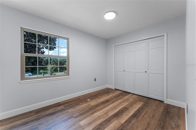 unfurnished bedroom featuring a closet, a textured ceiling, and dark hardwood / wood-style flooring