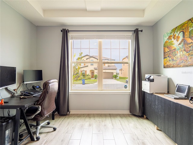 office space with a wealth of natural light, a tray ceiling, and light hardwood / wood-style floors