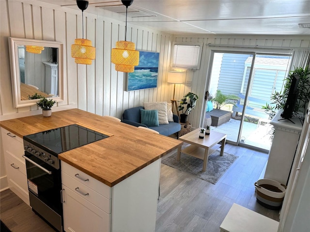 kitchen featuring wood walls, butcher block counters, decorative light fixtures, stainless steel range, and white cabinets