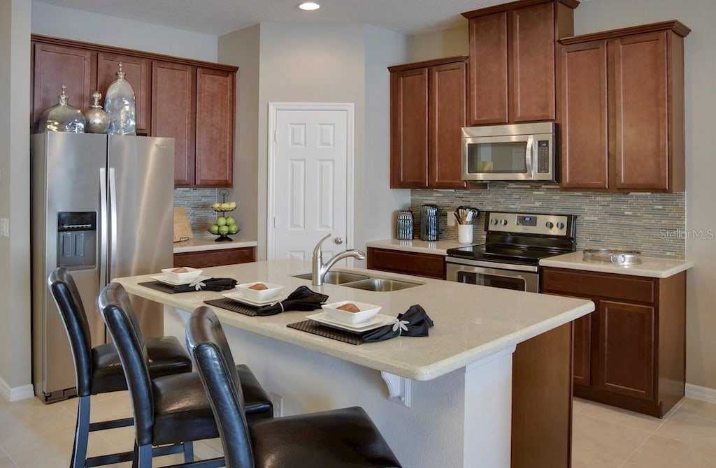 kitchen featuring decorative backsplash, a center island with sink, sink, a kitchen bar, and appliances with stainless steel finishes