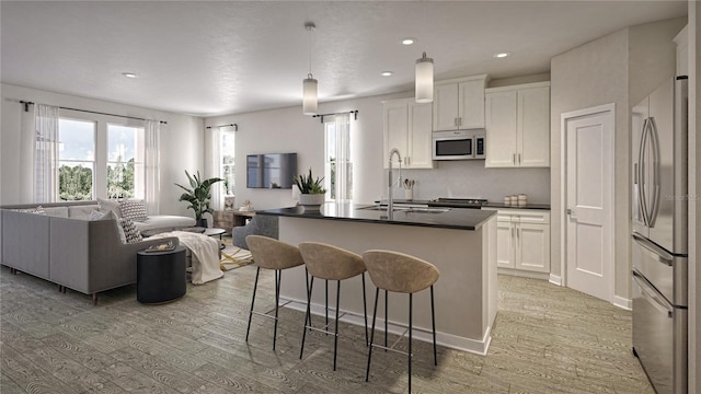 kitchen featuring white cabinets, hanging light fixtures, a center island with sink, light hardwood / wood-style floors, and stainless steel appliances