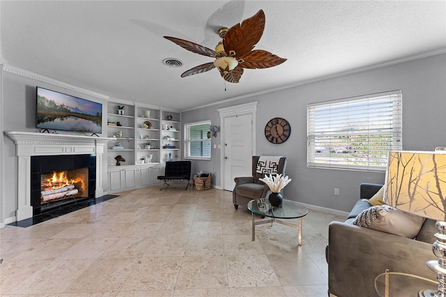 living room with built in features, a textured ceiling, a tile fireplace, ceiling fan, and ornamental molding