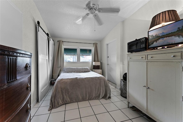 tiled bedroom with ceiling fan, a textured ceiling, vaulted ceiling, and a barn door