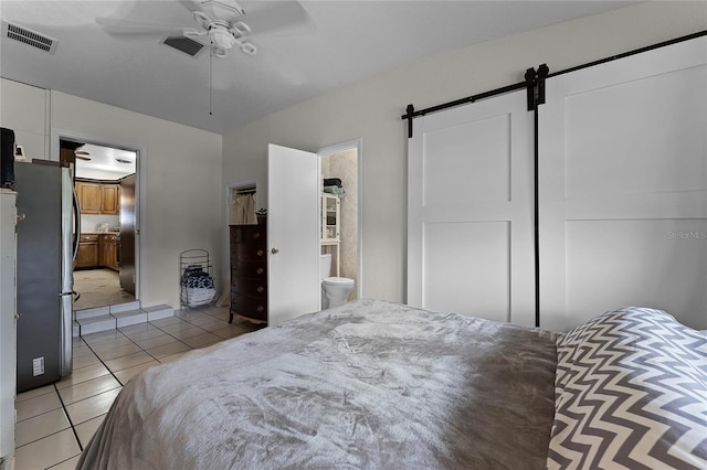 tiled bedroom featuring a barn door, stainless steel fridge, a closet, ceiling fan, and connected bathroom