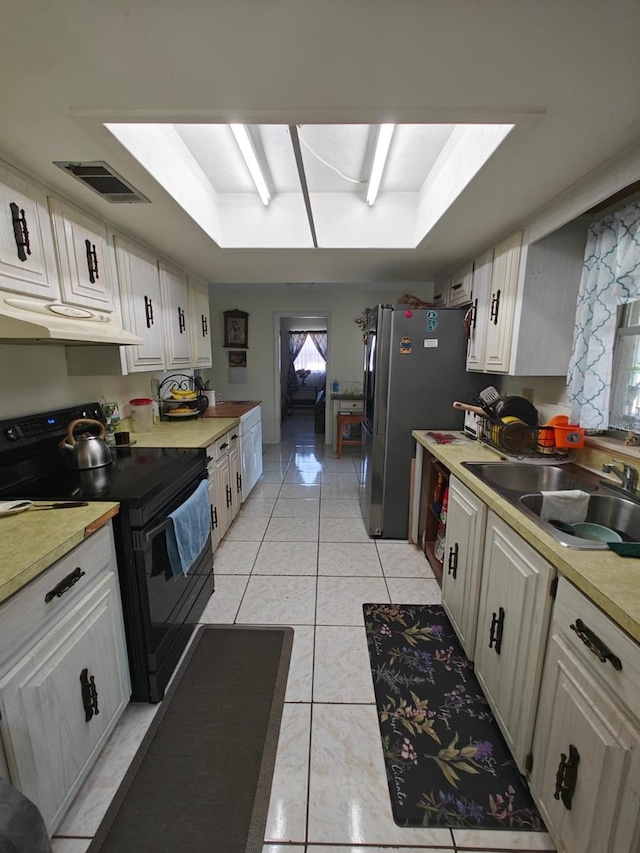 kitchen with black electric range oven, stainless steel fridge, white cabinets, light tile patterned floors, and sink