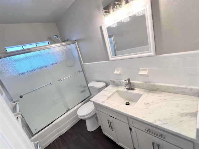 full bathroom with vanity, shower / bath combination with glass door, hardwood / wood-style flooring, tile walls, and toilet