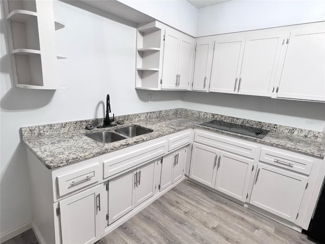 kitchen featuring white cabinets, light wood-type flooring, light stone countertops, and sink