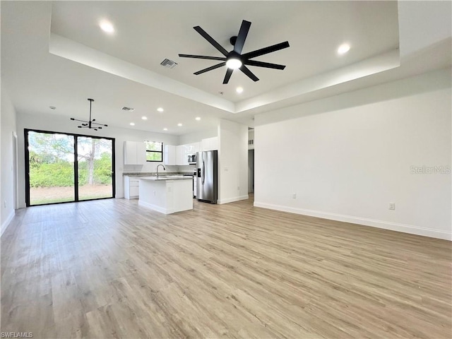 unfurnished living room with sink, a tray ceiling, light hardwood / wood-style floors, and ceiling fan