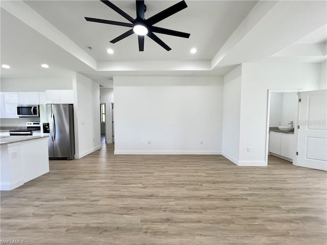 unfurnished living room featuring light hardwood / wood-style flooring, sink, a tray ceiling, and ceiling fan