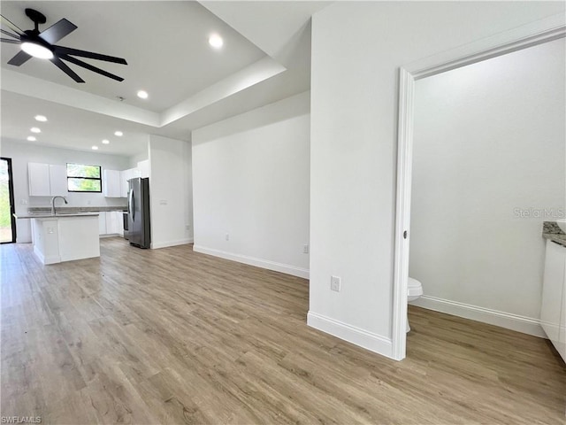 unfurnished living room featuring light hardwood / wood-style floors, sink, a raised ceiling, and ceiling fan