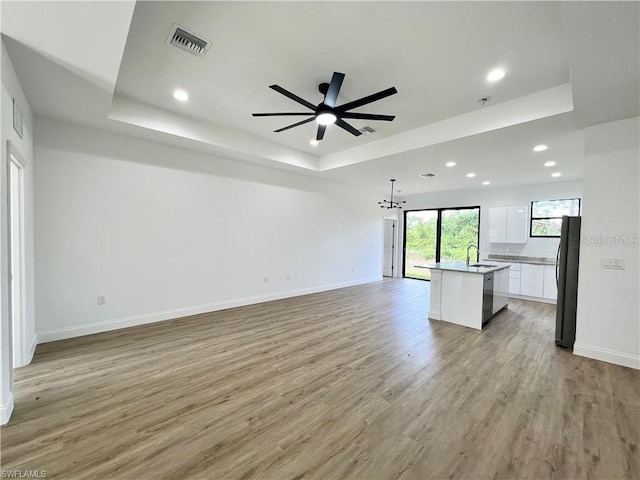 unfurnished living room with light hardwood / wood-style floors, sink, and a raised ceiling