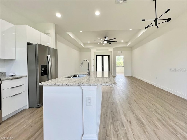 kitchen featuring an island with sink, a tray ceiling, stainless steel fridge, light wood-type flooring, and white cabinetry