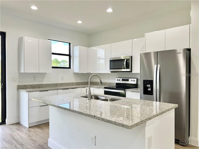 kitchen with sink, an island with sink, stainless steel appliances, and white cabinetry