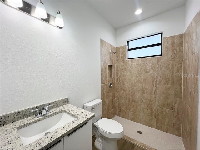 bathroom featuring toilet, vanity, and a tile shower