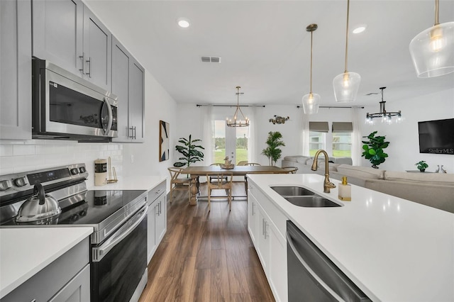 kitchen with dark wood-type flooring, gray cabinetry, stainless steel appliances, sink, and pendant lighting