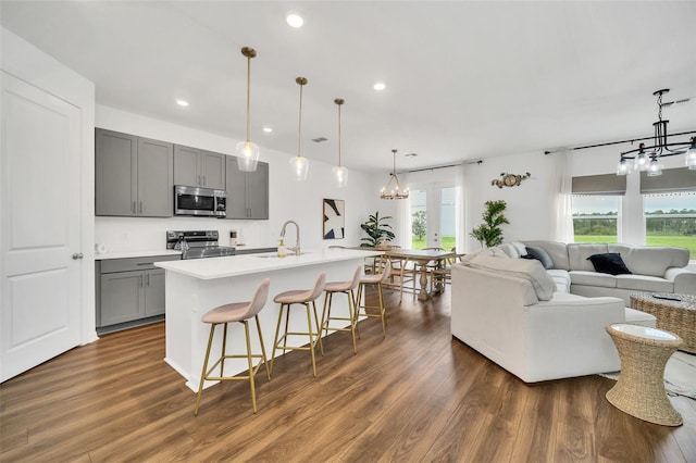 kitchen featuring gray cabinetry, stainless steel appliances, a center island with sink, a notable chandelier, and dark hardwood / wood-style flooring