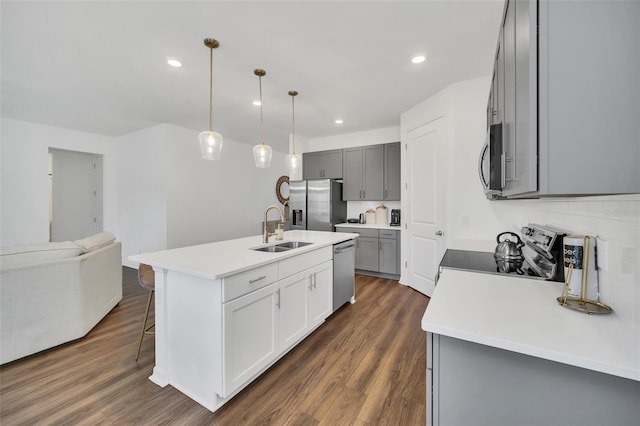 kitchen with dark hardwood / wood-style floors, stainless steel appliances, a center island with sink, sink, and pendant lighting