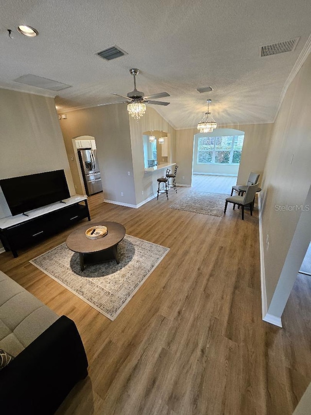 living room with hardwood / wood-style floors, ceiling fan with notable chandelier, a textured ceiling, and ornamental molding