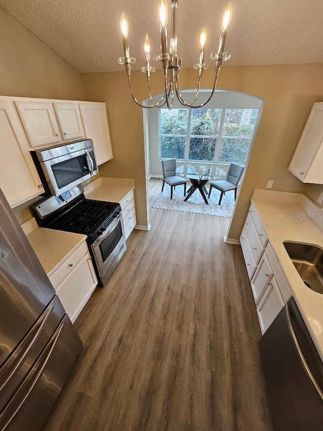 kitchen with stainless steel appliances, sink, decorative light fixtures, a notable chandelier, and white cabinets