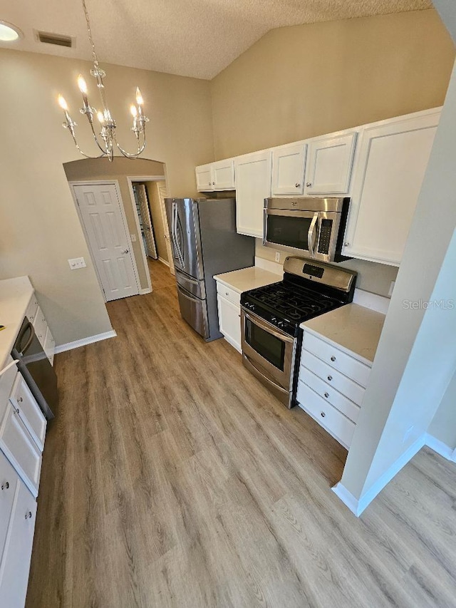 kitchen with a textured ceiling, stainless steel appliances, white cabinets, hanging light fixtures, and lofted ceiling