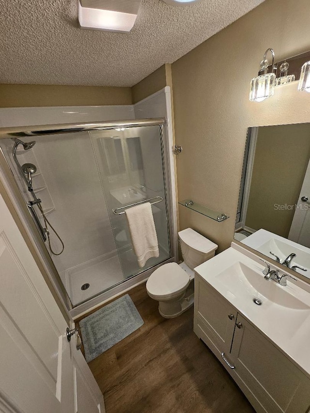 bathroom with walk in shower, vanity, a textured ceiling, hardwood / wood-style floors, and toilet