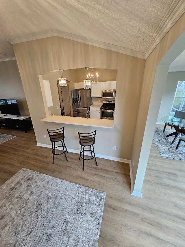 kitchen with white cabinets, a textured ceiling, appliances with stainless steel finishes, a kitchen bar, and kitchen peninsula