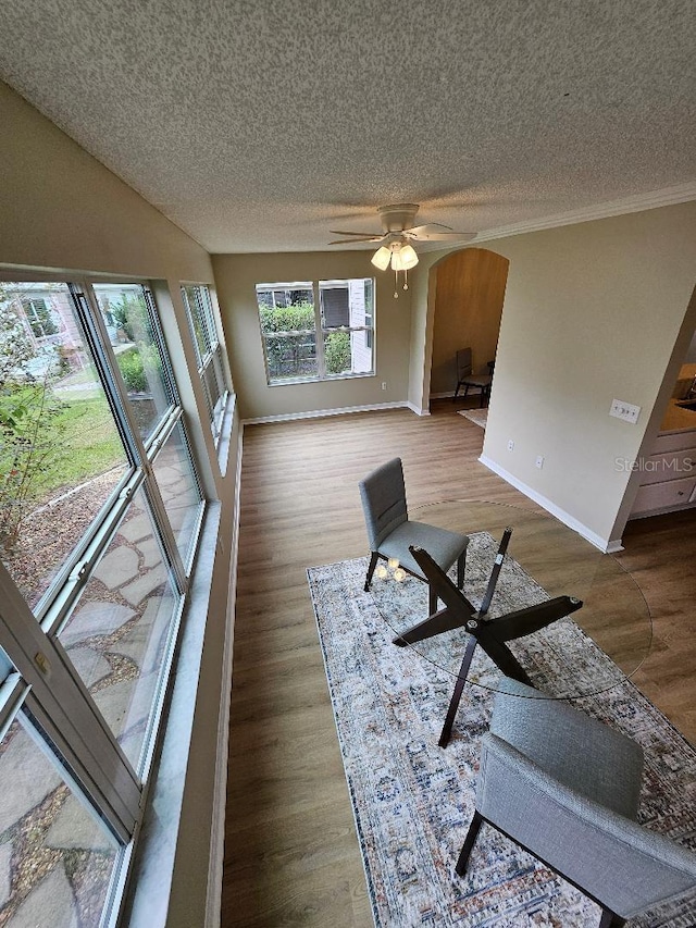 living room featuring hardwood / wood-style flooring, ceiling fan, ornamental molding, and a textured ceiling