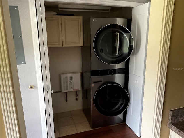 laundry area featuring stacked washer / drying machine, electric panel, tile patterned floors, and cabinets