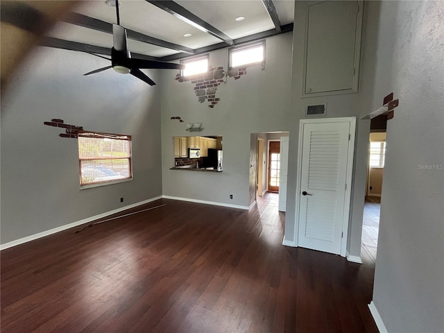 unfurnished living room with a towering ceiling, ceiling fan, beamed ceiling, and dark hardwood / wood-style floors