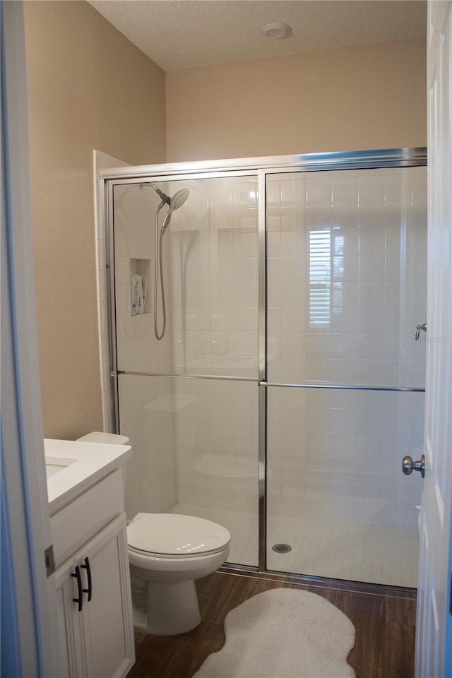 bathroom featuring hardwood / wood-style flooring, toilet, vanity, a textured ceiling, and walk in shower