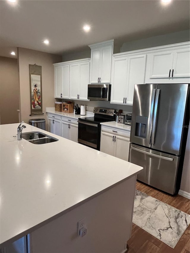 kitchen with a kitchen island with sink, dark wood-type flooring, stainless steel appliances, sink, and white cabinets