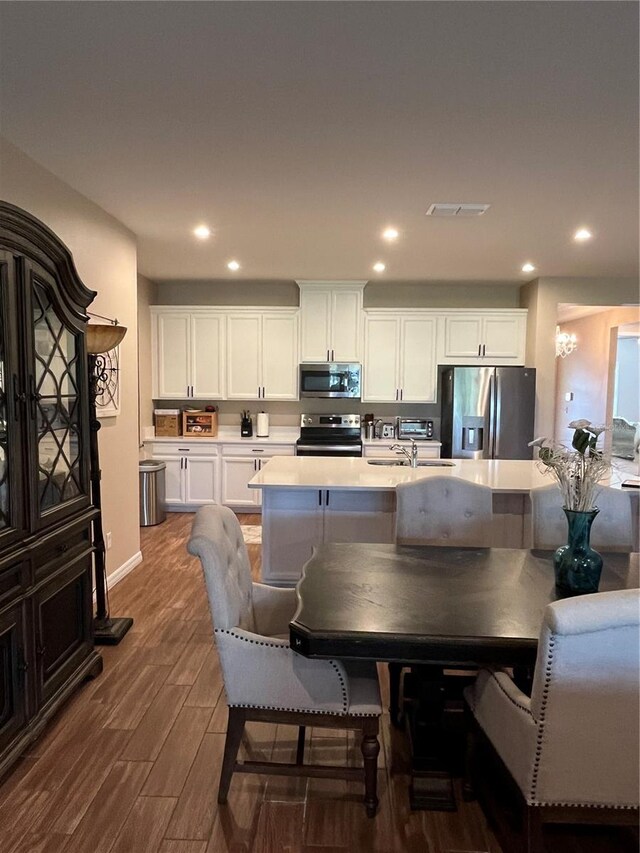 kitchen with white cabinetry, stainless steel appliances, dark hardwood / wood-style floors, a breakfast bar, and a center island with sink