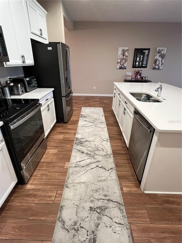 kitchen with an island with sink, appliances with stainless steel finishes, white cabinetry, dark wood-type flooring, and sink