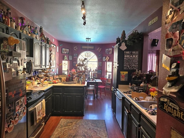 kitchen featuring dark wood-type flooring, appliances with stainless steel finishes, hanging light fixtures, and a textured ceiling