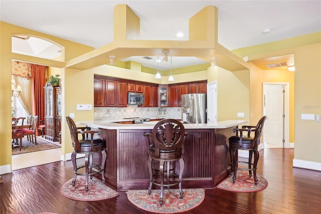 kitchen with a kitchen breakfast bar, kitchen peninsula, stainless steel appliances, and wood-type flooring