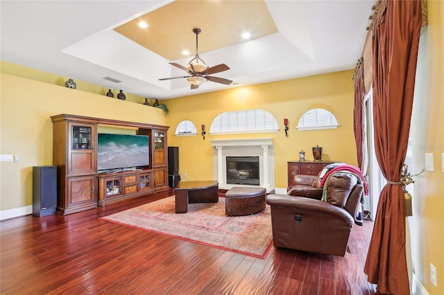 living room with ceiling fan, a tray ceiling, and dark hardwood / wood-style flooring