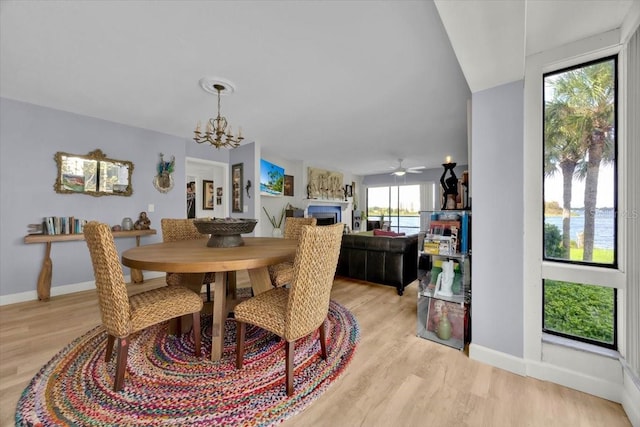 dining area featuring ceiling fan with notable chandelier, a water view, and light wood-type flooring