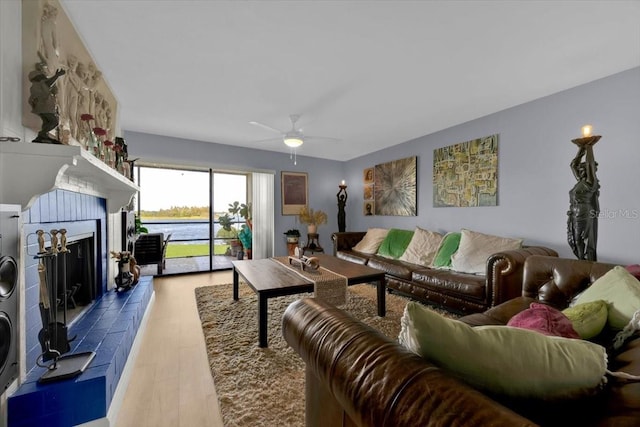 living room featuring hardwood / wood-style floors, a tiled fireplace, and ceiling fan