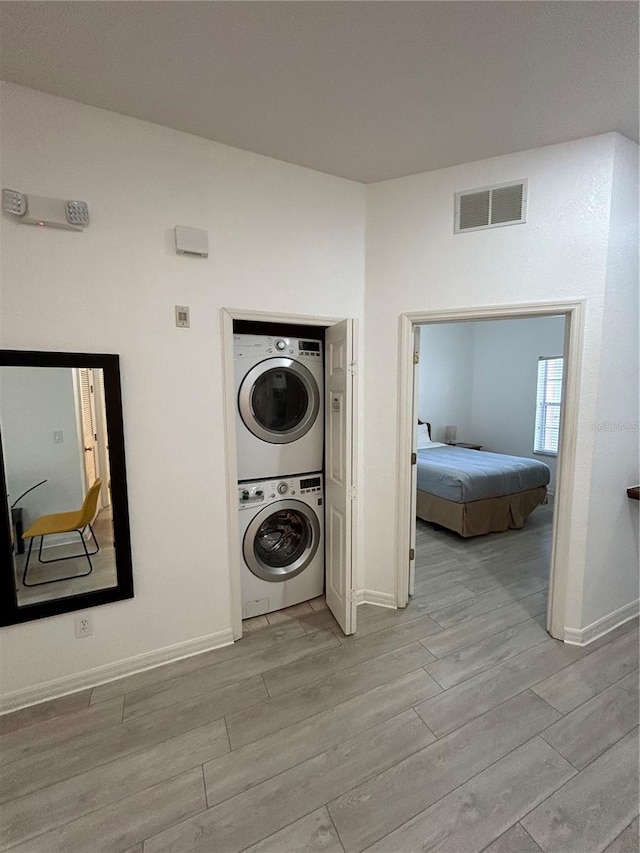 clothes washing area featuring light wood-type flooring and stacked washing maching and dryer